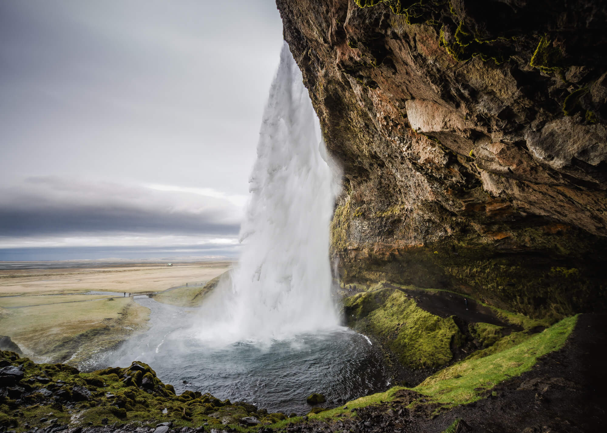 Achter de waterval Seljalandsfoss in IJsland met groen mos op de rotsen