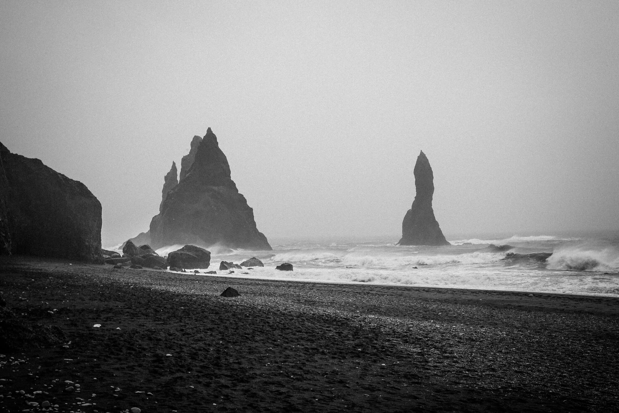 Zwart-witfoto van de rotspilaren Reynisdrangar bij het zwarte strand van Reynisfjara